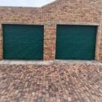 Two green roll-up garage doors installed on a brick building exterior