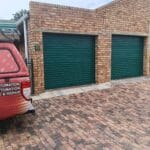 Two green roll-up garage doors installed on brick garage structure